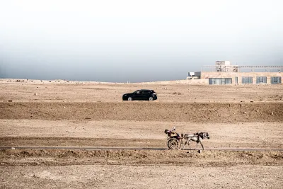 Carrozza trainata da un asino lungo una strada nel deserto egiziano, con un'automobile e un edificio moderno sullo sfondo